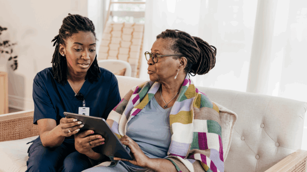 Black senior woman reviewing notes on a tablet with a caregiver