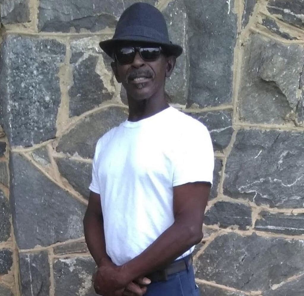 Man wearing hat and sunglasses, standing outside.