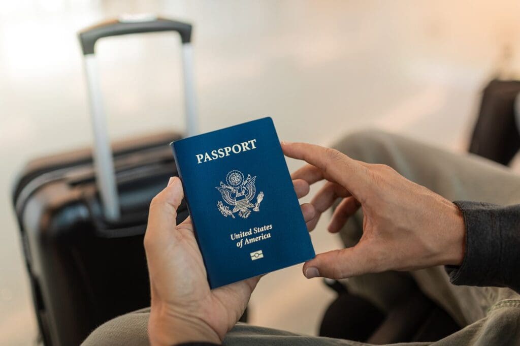 Hands holding a US passport a suitcase in the background