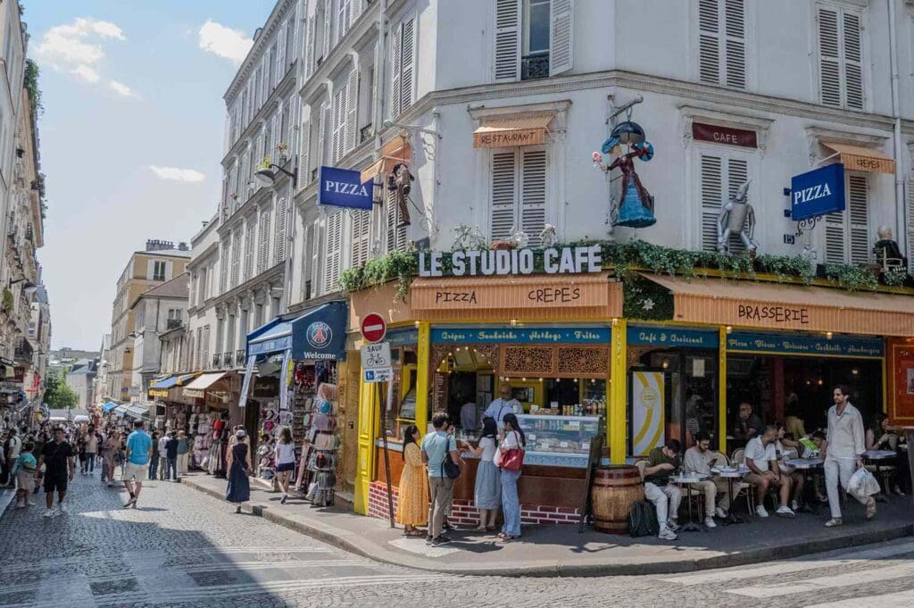 I’m a Paris Local and This Is the Most Important Etiquette Tip to Know When Visiting France Street view of a caf corner in Montmartre Paris with pedestrians and outdoor seating areas