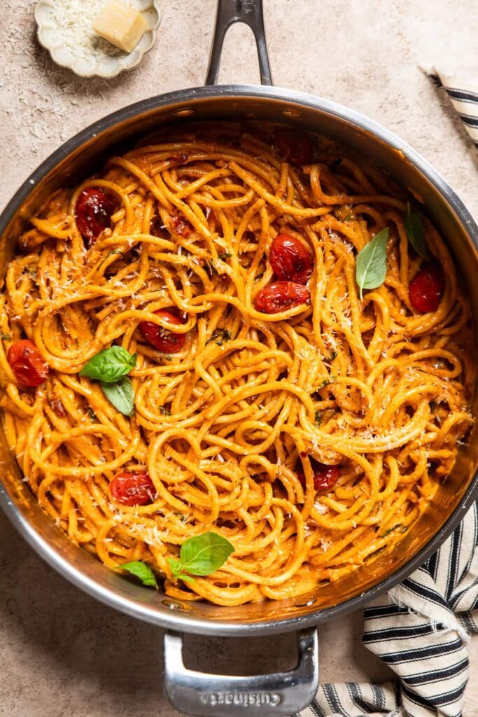 a stainless steel skillet with roasted tomato and garlic sauce over long pasta noodles.