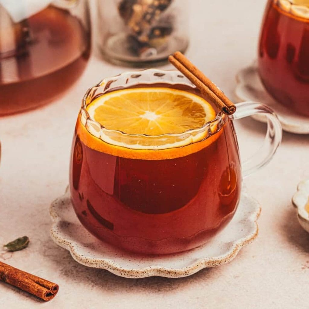 A glass of chai vanilla bean hot toddy with cinnamon sticks surrounding it.