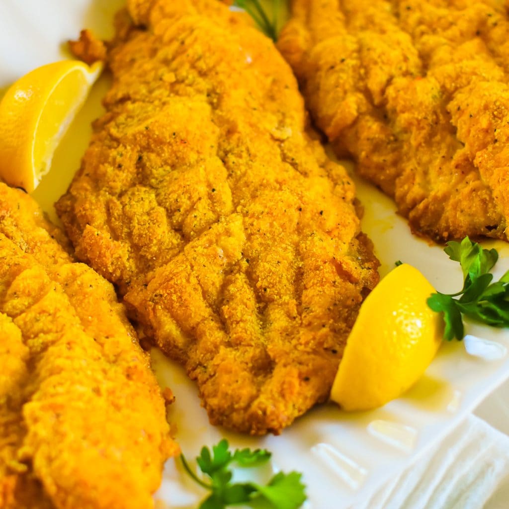 Crunchy Stove Baked Catfish (Quick and Easy!) golden brown crispy oven baked catfish fillets on a platter with fresh parsley and lemon wedges.