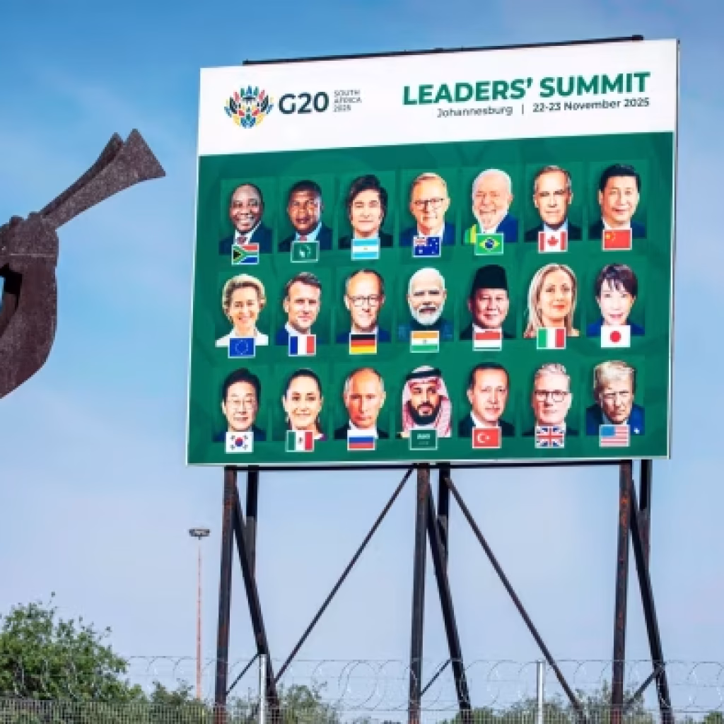 A billboard shows portraits of G20 leaders with their national flags ahead of the 2025 G20 Summit in Johannesburg. A metal silhouette sculpture of a person blowing a horn is in the foreground.