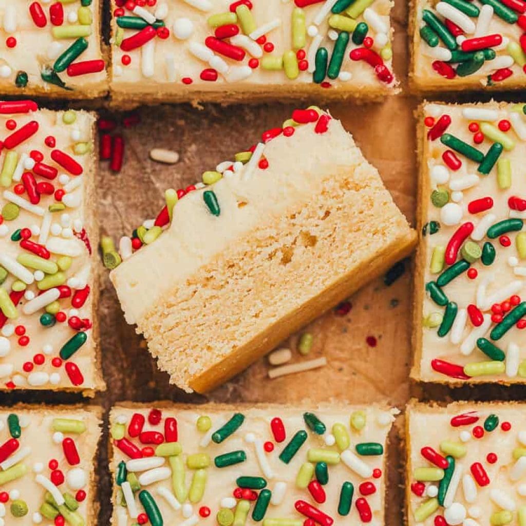 Frosted sugar cookie bars sliced showing the top of the bar with sprinkles. One bar is flipped on its side showing the bar and the thick frosting.