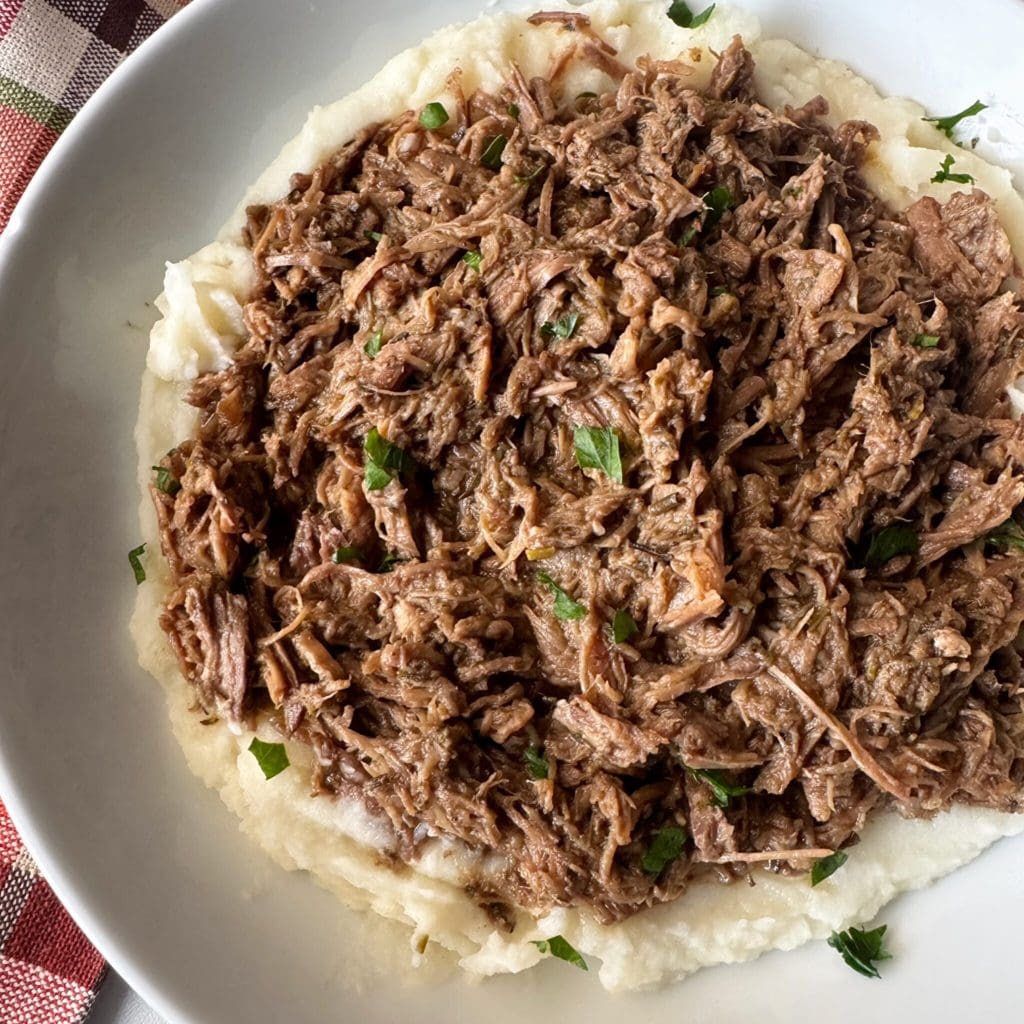 overhead shot of shredded beef served over mashed potatoes on a white plate
