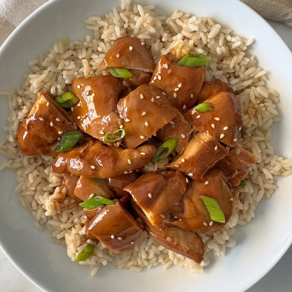 overhead shot of teriyaki chicken served over white rice garnished with green onion and sesame seeds