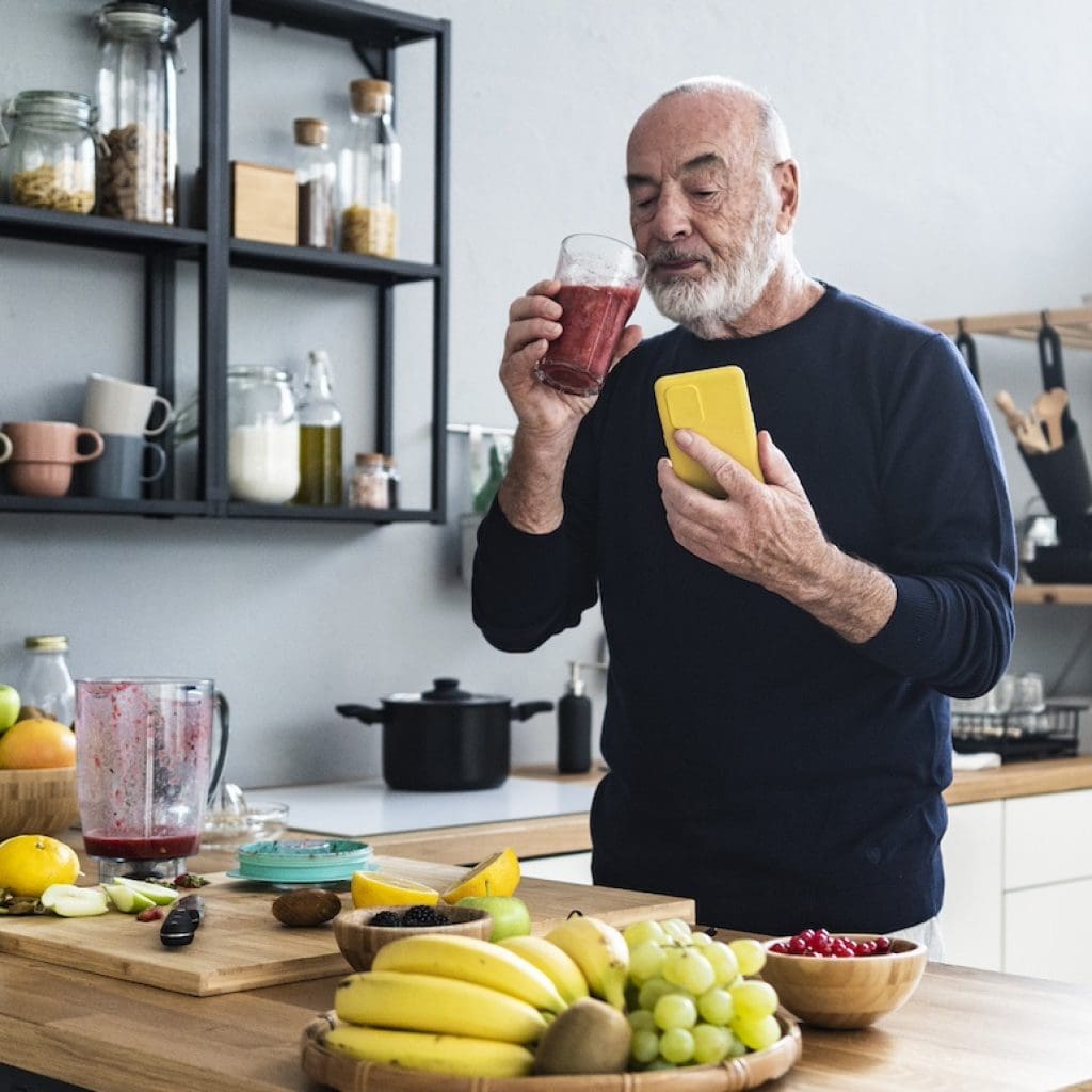 Senior man with smartphone making healthy smoothie at home