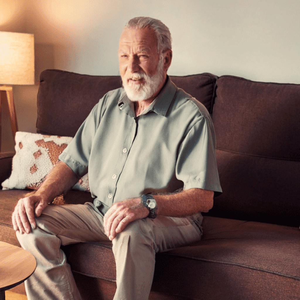 Senior man sitting on a couch with a voice-activated device onthe coffee table