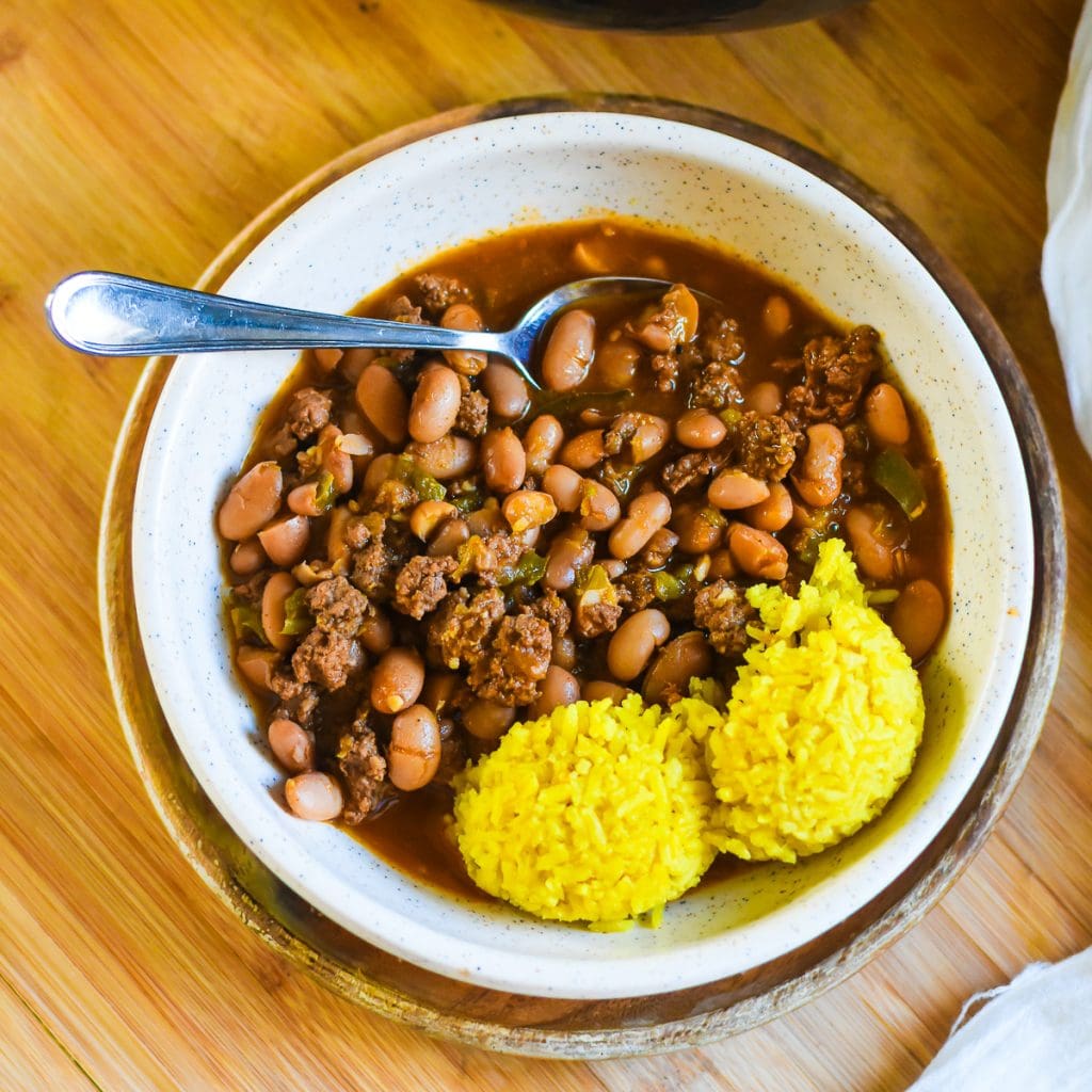 bowl of ground beef and pinto beans cooked in broth and aromatics with two scoops of homemade yellow rice.