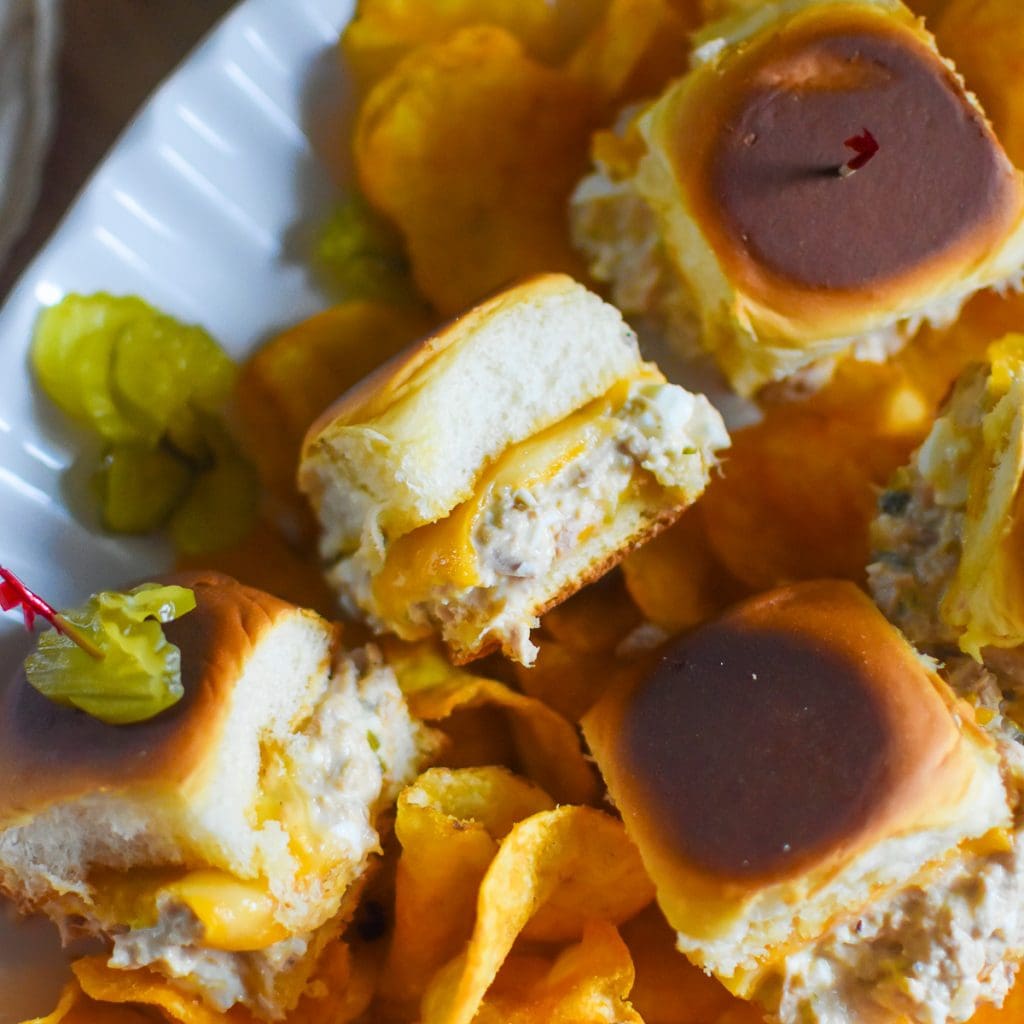 classic tuna melt recipe served on toasted Hawaiian slider buns on platter with pickle slices and seasoned potato chips.