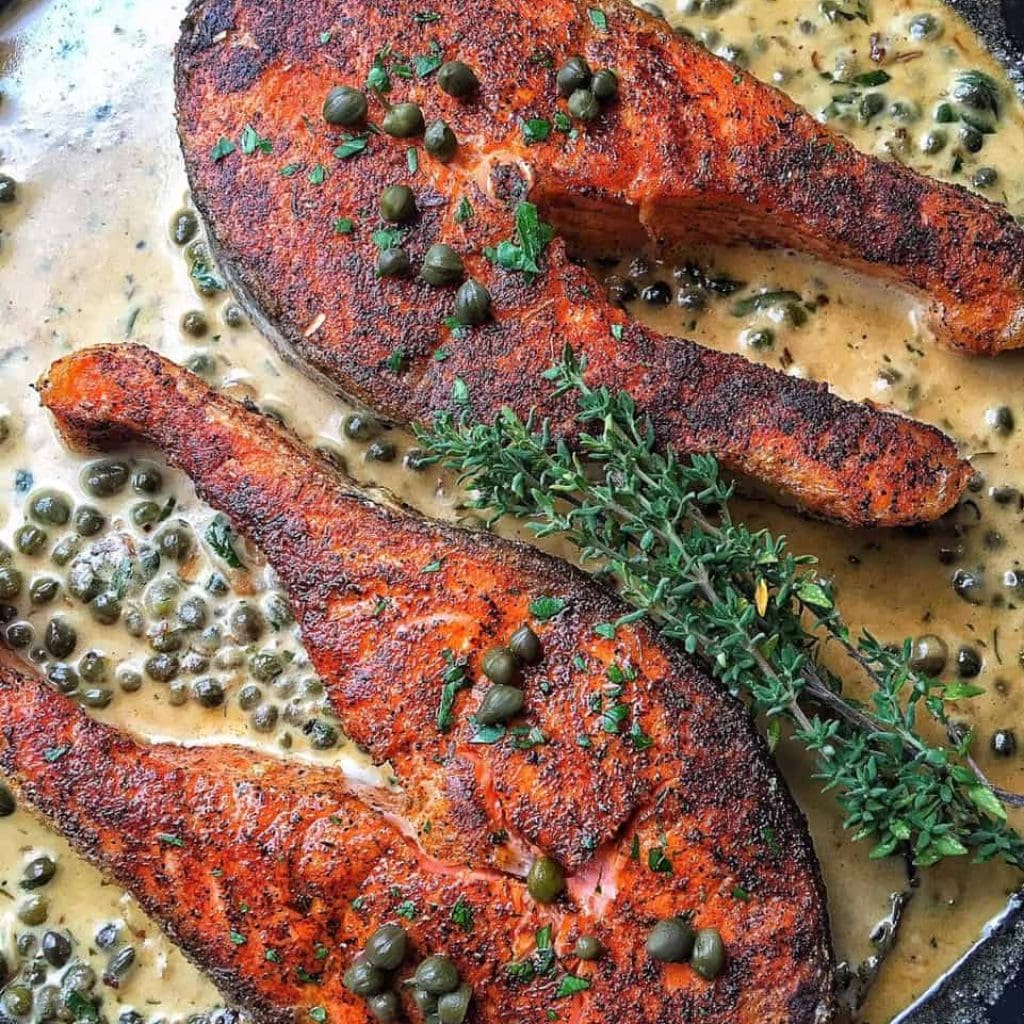 Seasoned salmon fillets cooked with fresh herbs on a baking sheet.