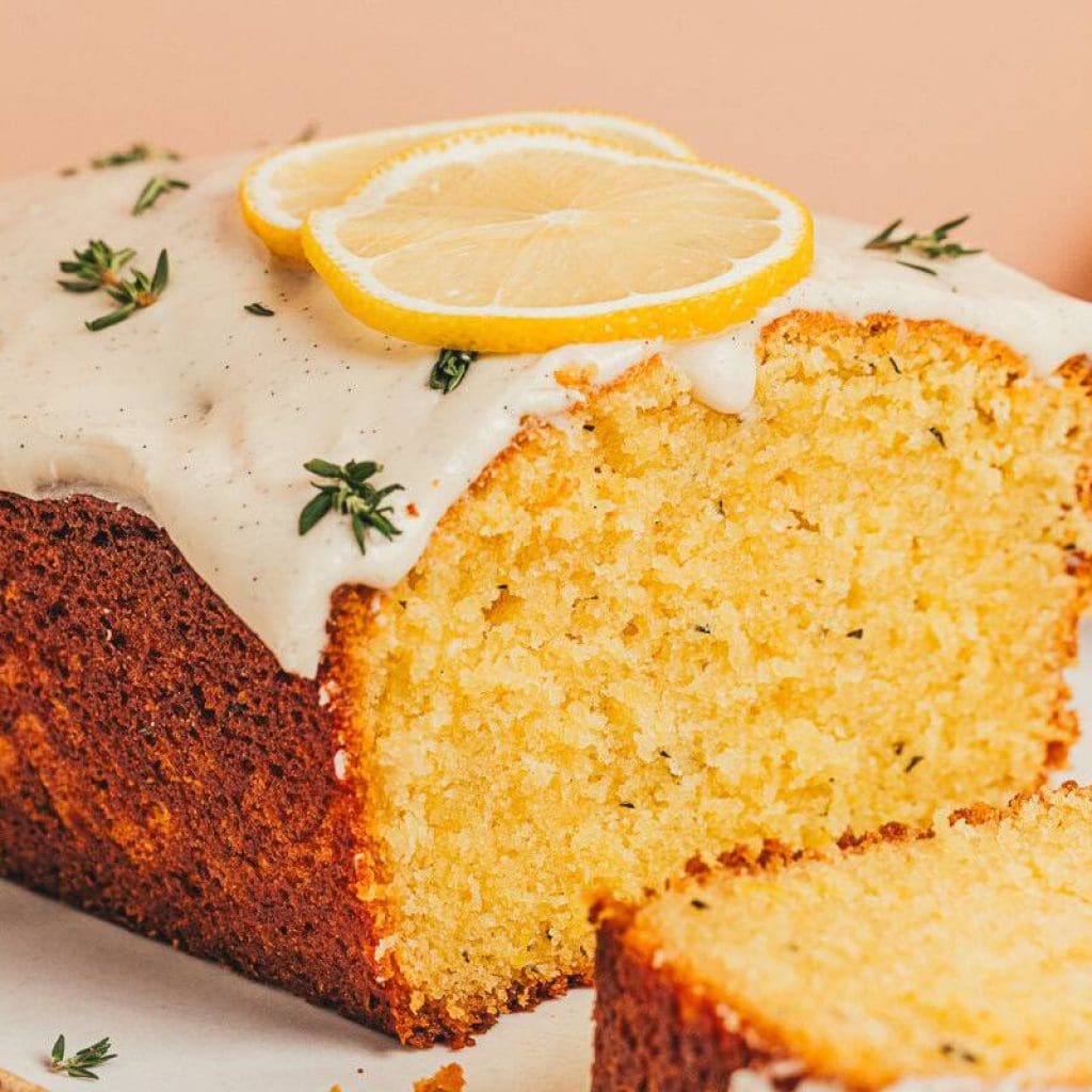 A lemon Thyme cake loaf cut into slices on a platter.