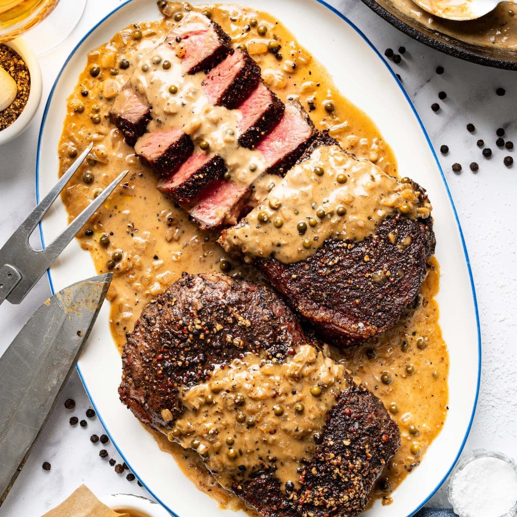 Seared steak slices with creamy peppercorn sauce on a white plate.