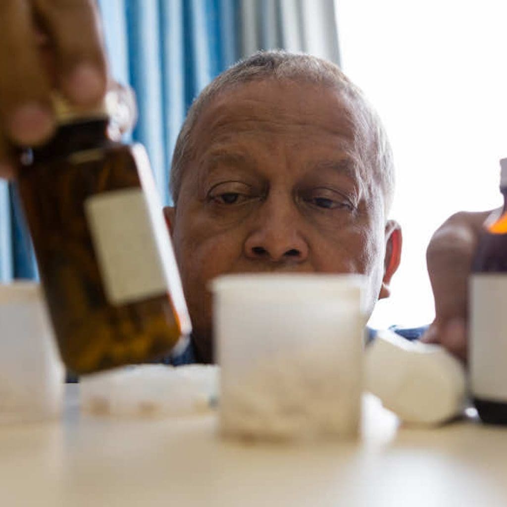 Senior man reaches for medication bottle on shelf next to other medications