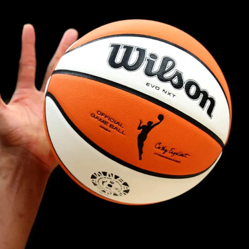 A hand holding a Wilson basketball against a black background.
