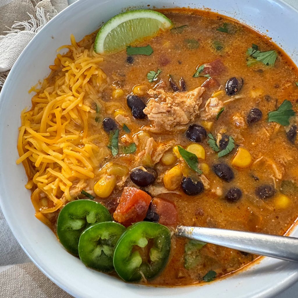 overhead shot of Crockpot Chicken Enchilada Soup in a white bowl garnished with jalapeno, cheese, and sliced lime