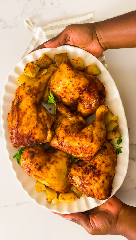 35+ Soul Food Sunday Dinner Ideas Your Family Will Love brown hands holding a platter of crispy baked southern chicken with potatoes, onions, and parsley for Soul Food Sunday dinner.