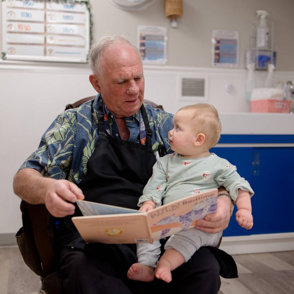 Retirees Are Helping Child Care Centers While Connecting with Community Older man reading a book to a baby