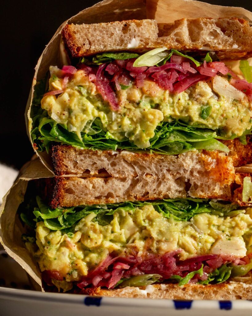 Close up of a sandwich cut in half to reveal the layers of lettuce, chickpea salad, and sumac onions.