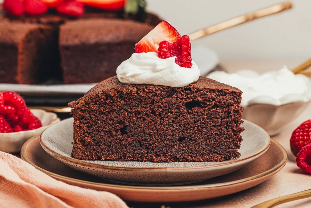 A slice of chocolate ricotta cake with whipped cream and berries on a plate.