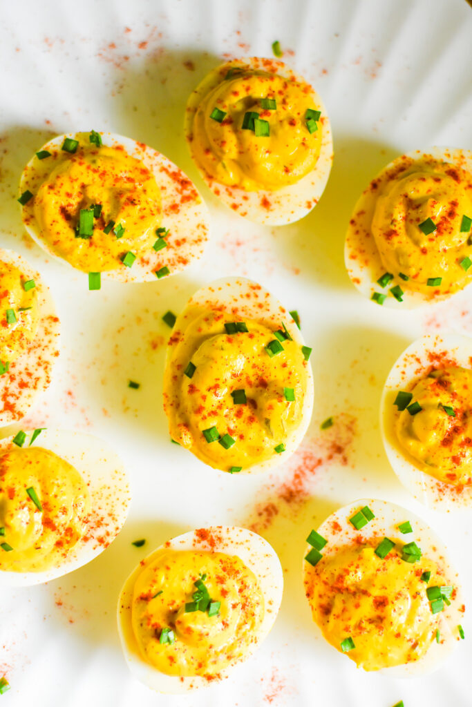the best southern deviled eggs ever on a white platter sprinkled with diced green chives and smoked paprika powder.