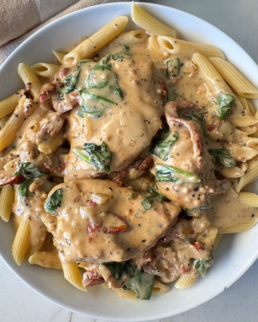 Slow Cooker Tuscan Chicken – Fit Slow Cooker Queen overhead shot of Tuscan chicken on a white plate served over penne pasta
