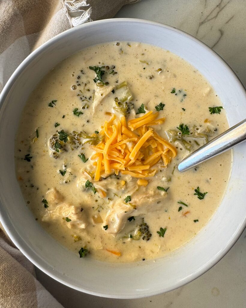 Crockpot Chicken Broccoli Cheese Soup overhead shot of slow cooker Chicken Broccoli Cheese Soup in a white bowl garnished with shredded cheddar cheese