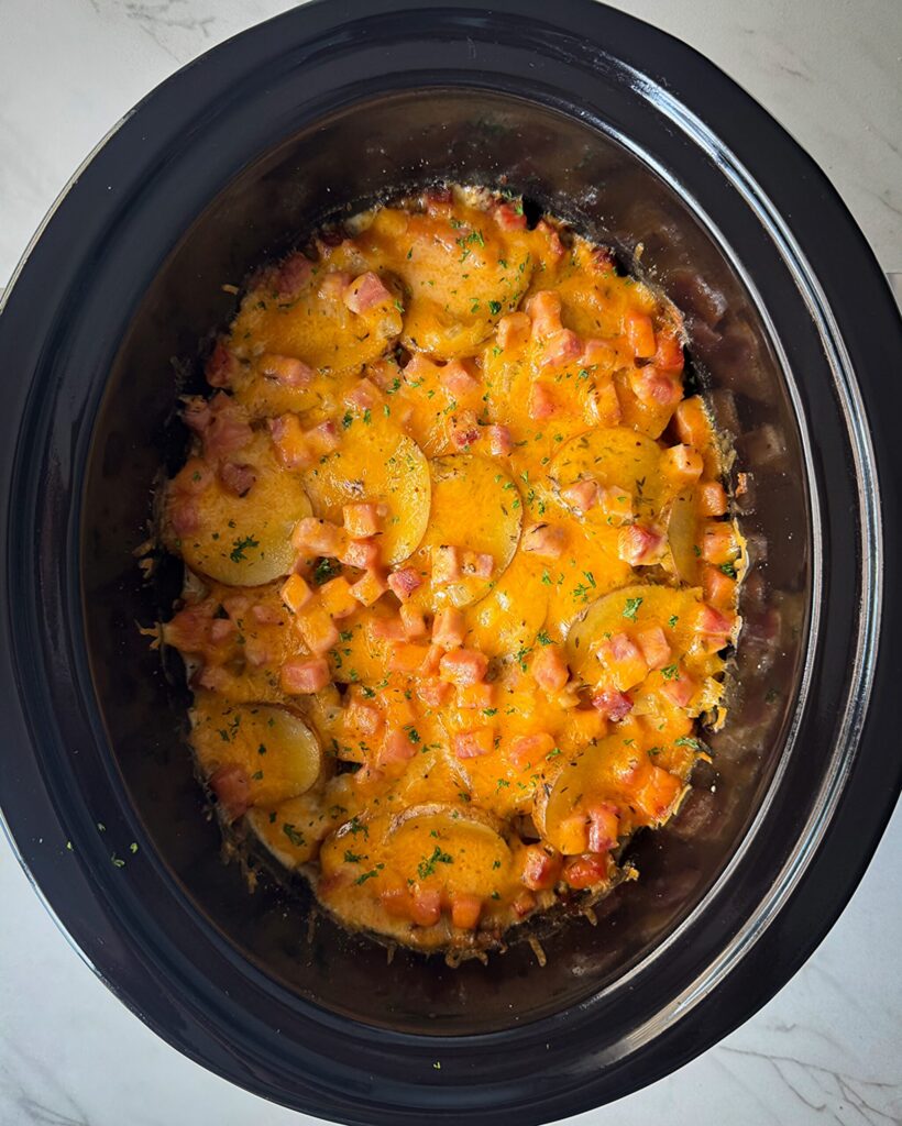 Crockpot Scalloped Potatoes and Ham overhead shot of cooked Scalloped Potatoes and Ham in a black slow cooker