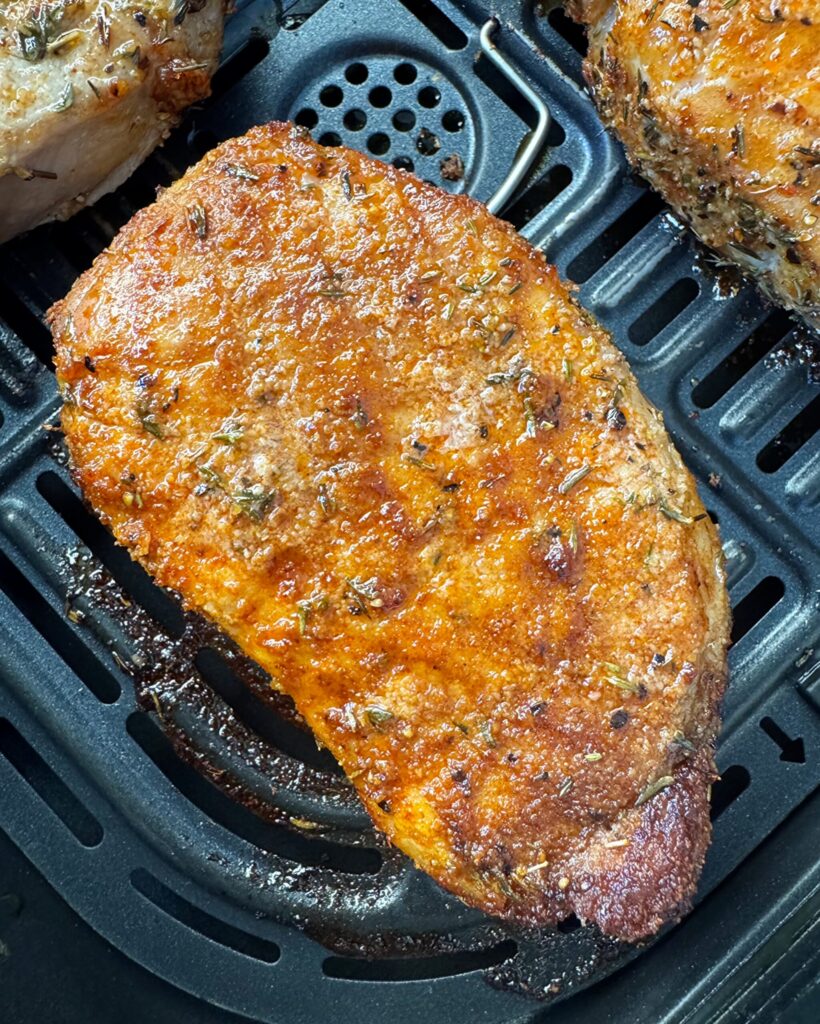 Easy Air Fryer Pork Chops close up shot of 1 cooked pork chop in a black air fryer