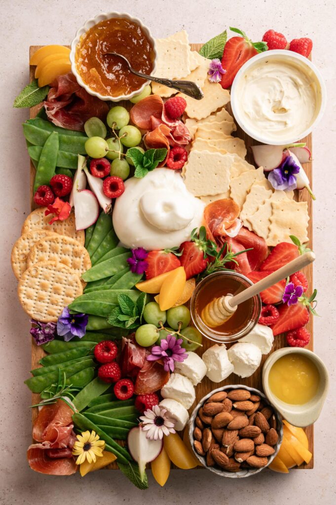 Spring charcuterie board with burrata, brie, fresh fruit, and edible flowers