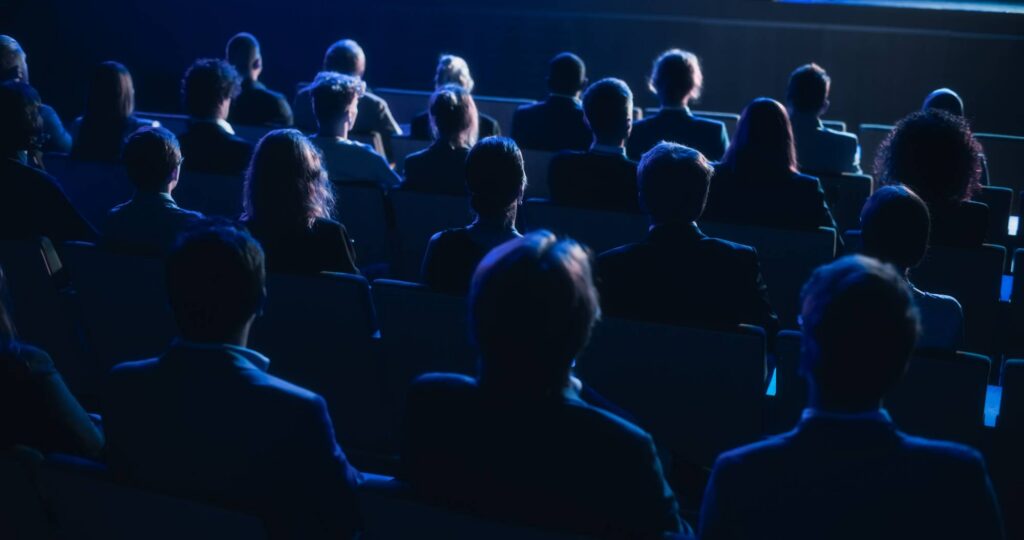 Is Everyone Using AI? How False Perceptions Can Become Self-fulfilling Rear view of audience in a darkened room