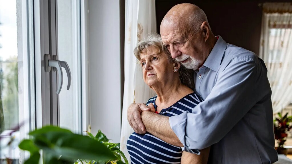 One Partner’s Dementia May Predict the Other’s Future Risk A photo of a senior man hugging his wife in front of a window in their home.