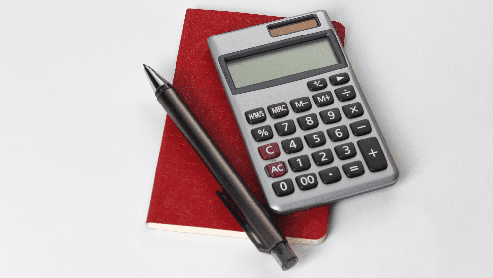 Here’s How to Avoid the Capital Gains Tax on Your Home Sale A person writing on a notepad and using a calculator to see how to avoid capital gains tax.