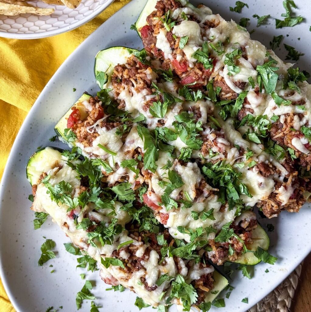 Taco Stuffed Zucchini Boats with Ground Beef and Rice Zucchini halves stuffed with ground beef and rice topped with melted cheese and fresh cilantro on a platter.