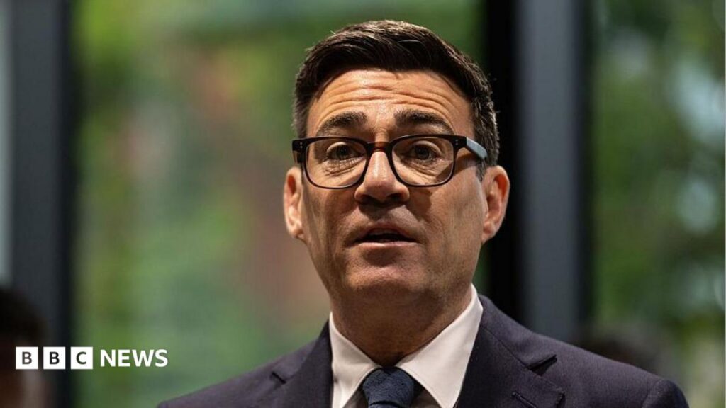 Andy Burnham to address social care, youth unemployment and devolution A picture of Andy Burnham from the shoulders up. He is wearing a dark suit with a white shirt and dark tie, has thick-rimmed black glasses on, and has short, dark brown hair. The background behind him is blurred and he is looking forward with his mouth slightly open and his eyebrows raised.