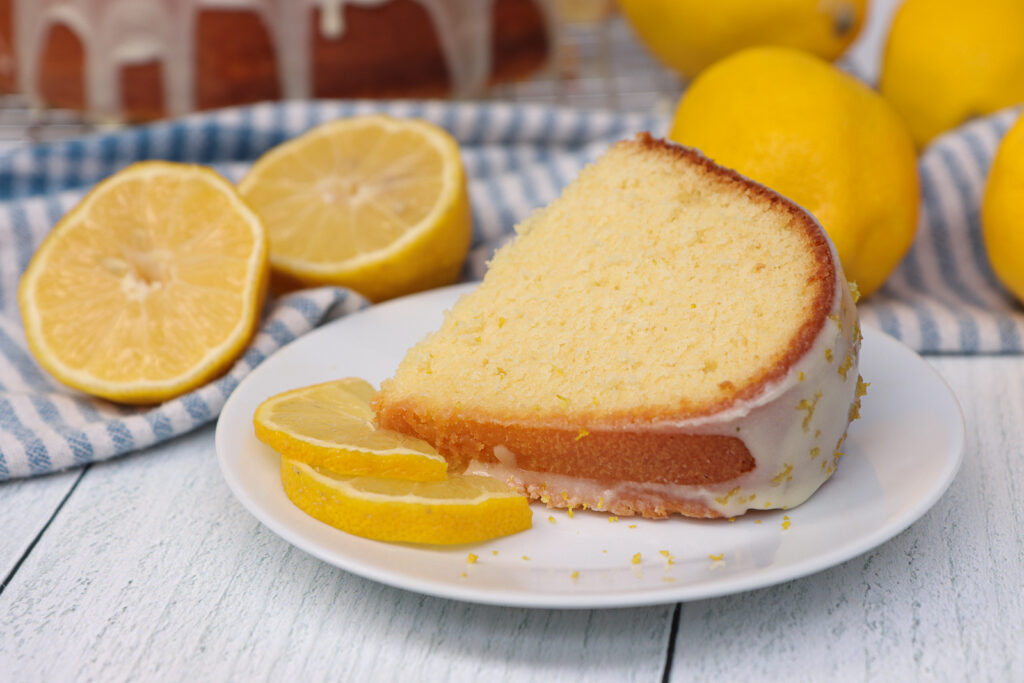 Lemon Pound Cake Recipe (Moist & Full of Real Lemon Flavor) A slice of lemon pound cake on a place with a lemon glaze and lemon zest garnish.