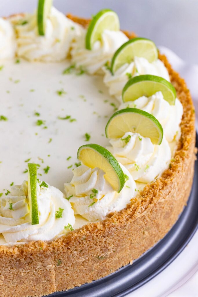 No-Bake Key Lime Cheesecake with Mascarpone Key lime cheesecake with a graham cracker crust. The top of the cheesecake is decorated with piped whipped cream and half slices of key lime on top of the whipped cream